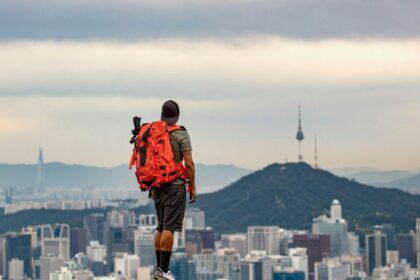 man in orange jacket and brown pants standing on rock during daytime