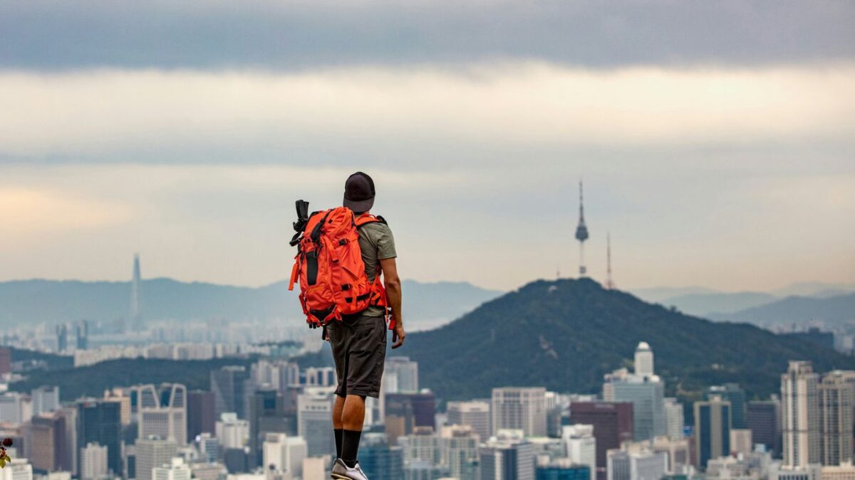 man in orange jacket and brown pants standing on rock during daytime