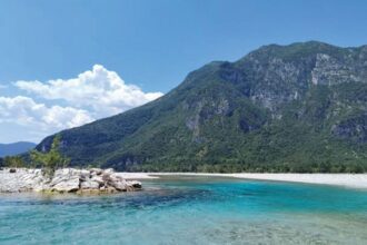 A turquoise river flows before a mountain.