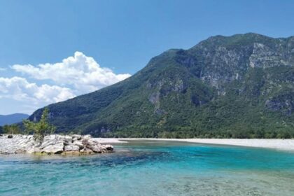 A turquoise river flows before a mountain.