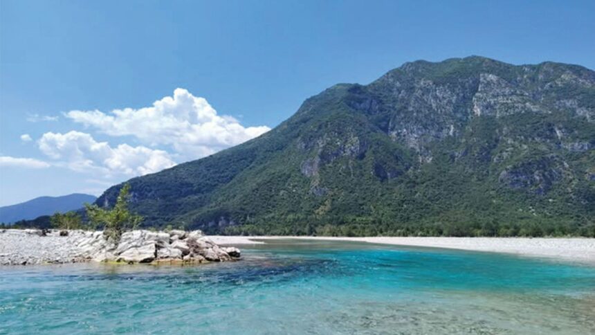 A turquoise river flows before a mountain.