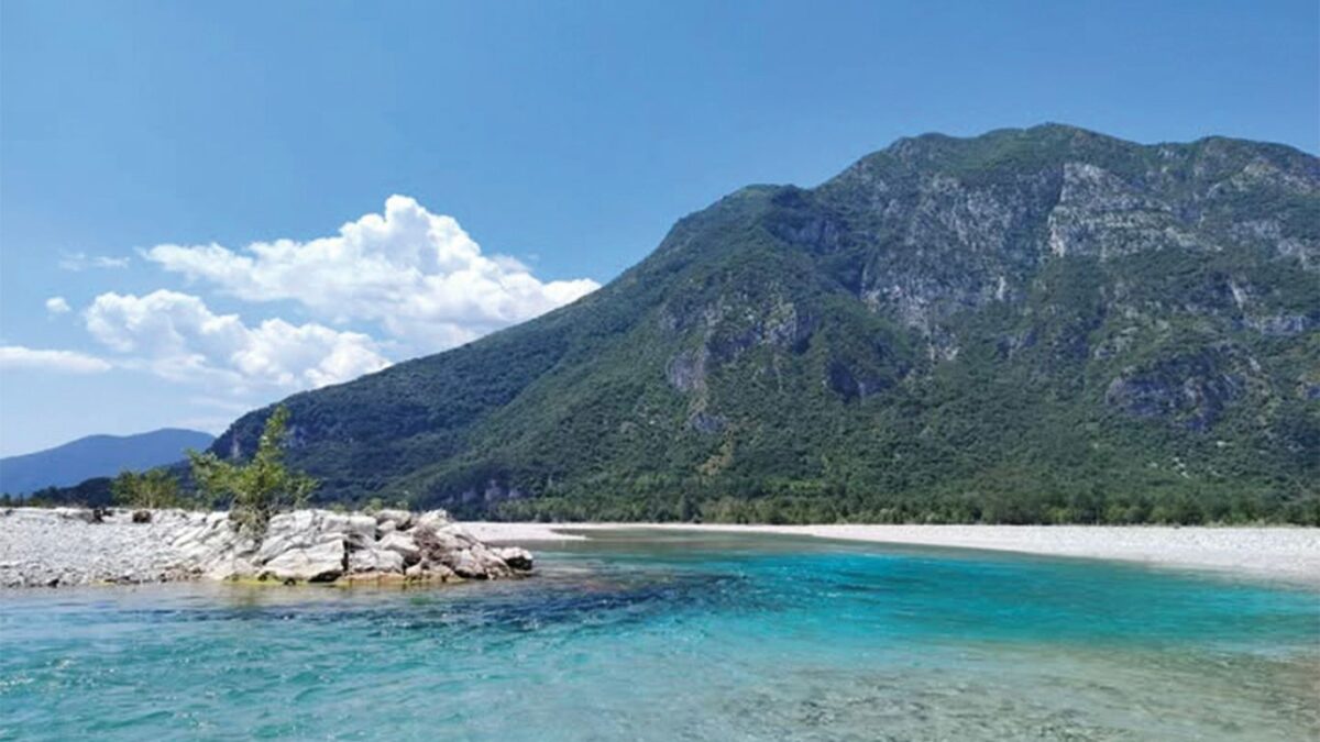 A turquoise river flows before a mountain.